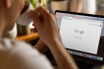 Persoon achter laptop die kop koffie drinkt en Google bezoekt